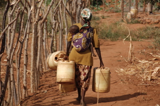 A woman carries four jerricans, and her child, to the community’s new water well. 