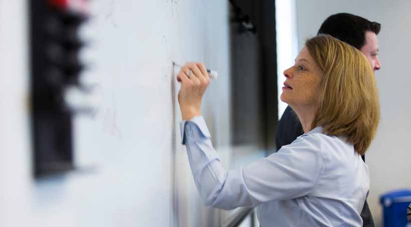 student writes on white board in class