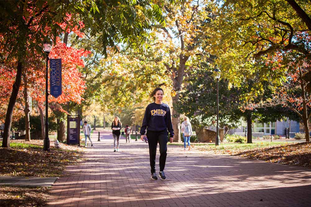 student walking on campus with fall leaves in background