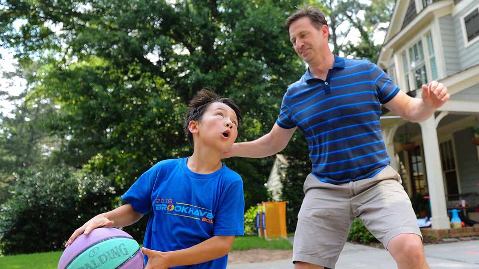 father and son in blue shirts playing basketball outside their home