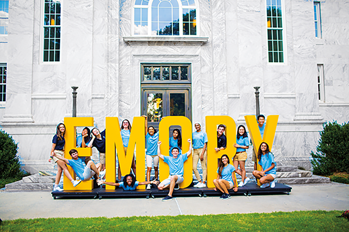 Students in blue t-shirts and shorts pose in and around large yellow letters spelling Emory