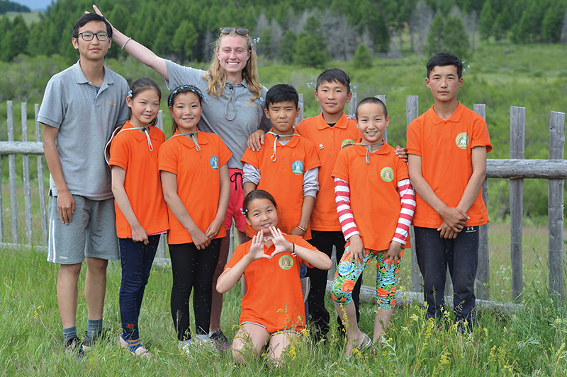 A woman and a man stand with a group of children wearing matching bright orange shirts.