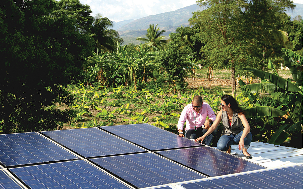 Sandra Kwak and another person, both in sunglasses, kneel to inspect a solar panel in a tropical setting