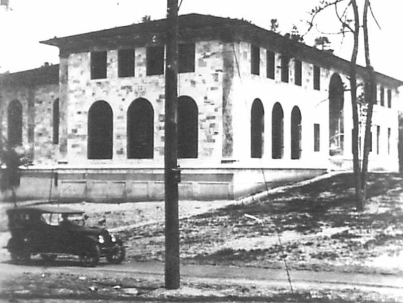 A black and white photo from 1920 of the Theology Building, including a Model T Ford car driving in front of the marble structure with several arched windows 