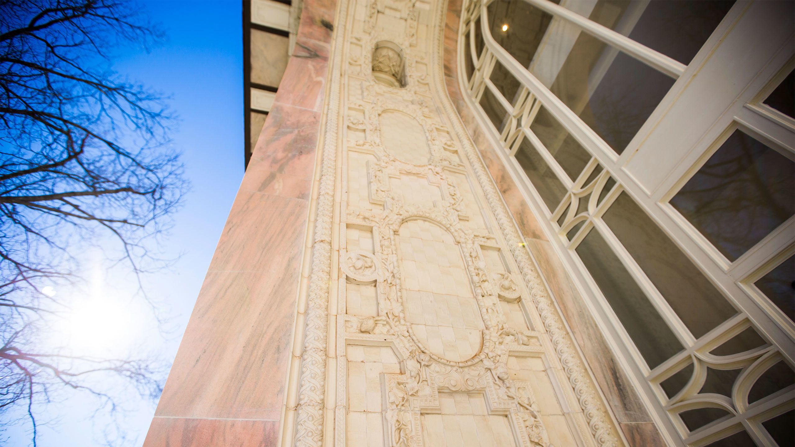 A close-up of the detailed carvings in the marble lining the arched windows outside of the building