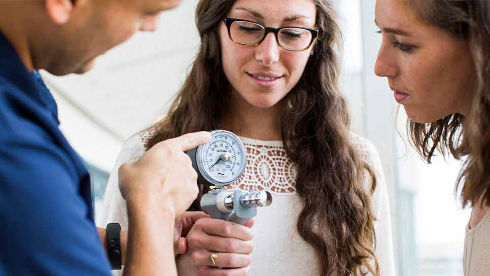 professor showing two women students a gauge as one student holds it