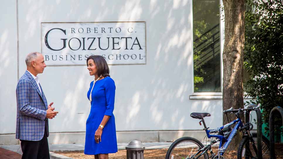 man and woman faculty talking outside by school sign