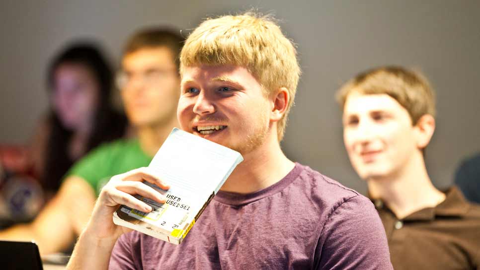 student in class holding book, smiling, and enjoying class discussion