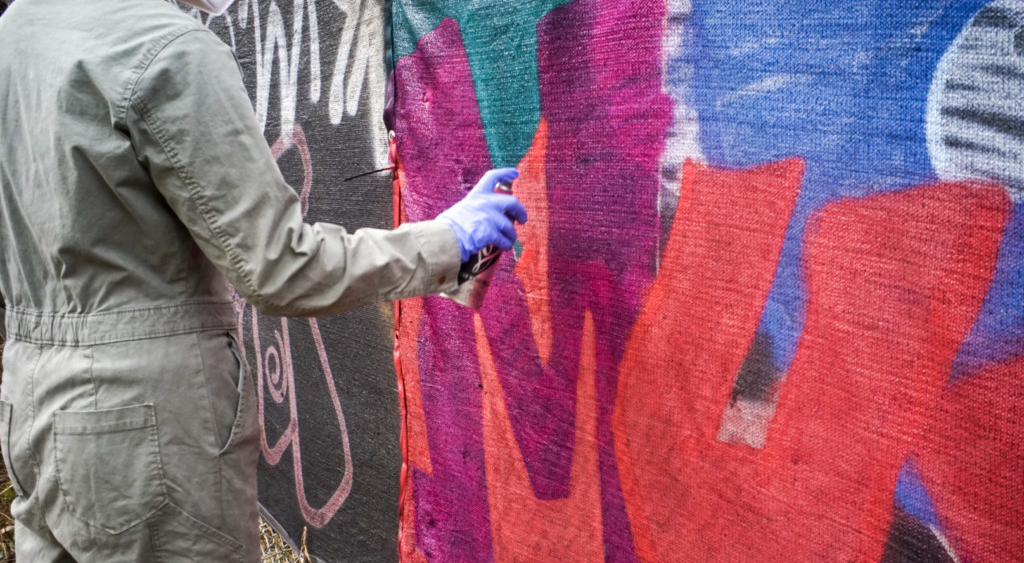 A man in a suit spray-paints graffiti on a wall.