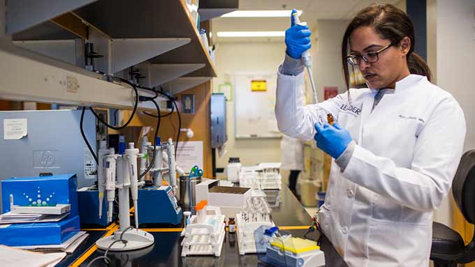 scientist with blue gloves squirting a syringe into a test tube