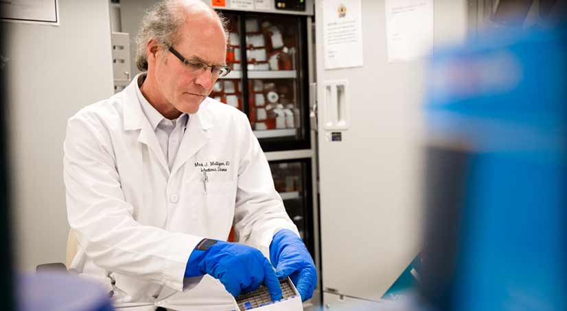 scientist in a lab wearing a white coat and blue gloves