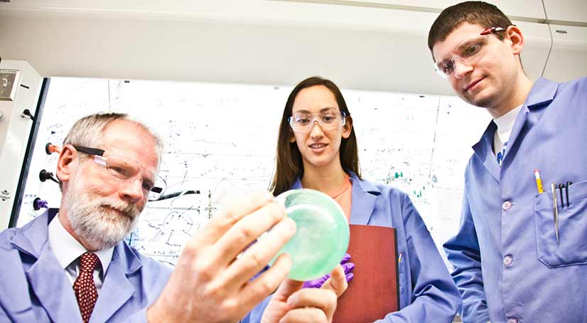 professor showing two students an experiment in a lab