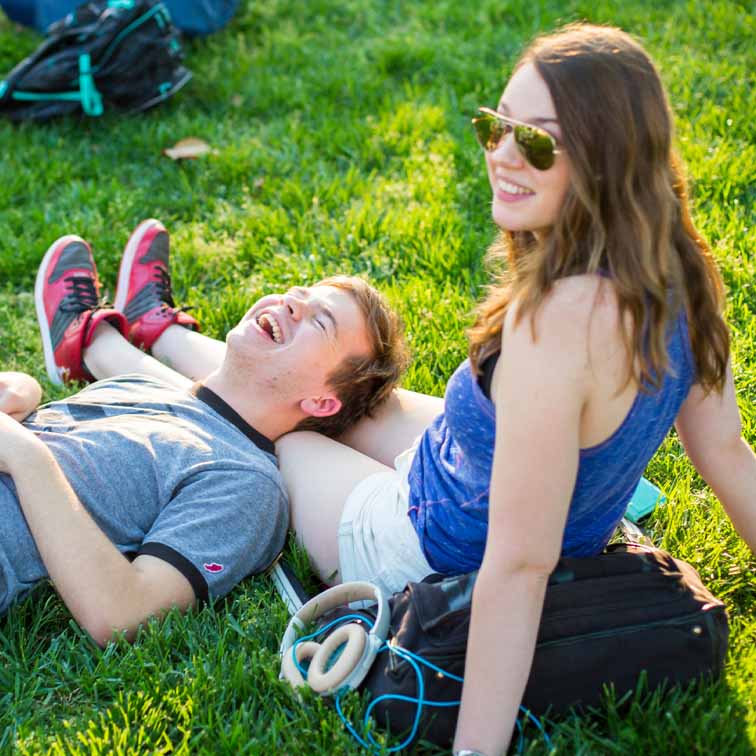 male and female student on grass with his head resting across her knees