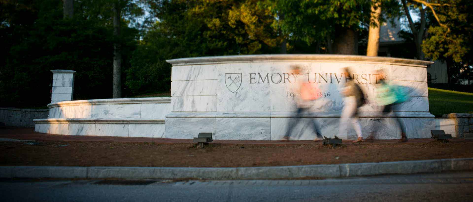 students walking in front of the marble wall that says emory university