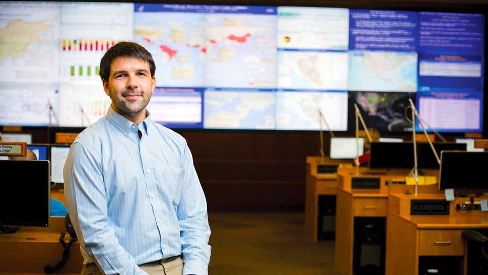 man stands in classroom with desks and world maps