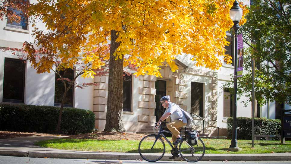 student with bike on quad with fall leaves in background