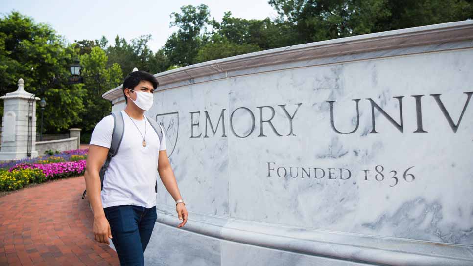 student wearing a mask walking by emory entrance