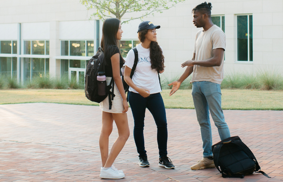 three students with backpacks talking in front of Emory building between classes