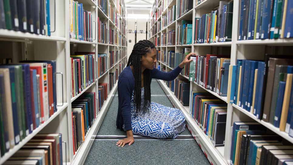 student sitting on floor in library stacks
