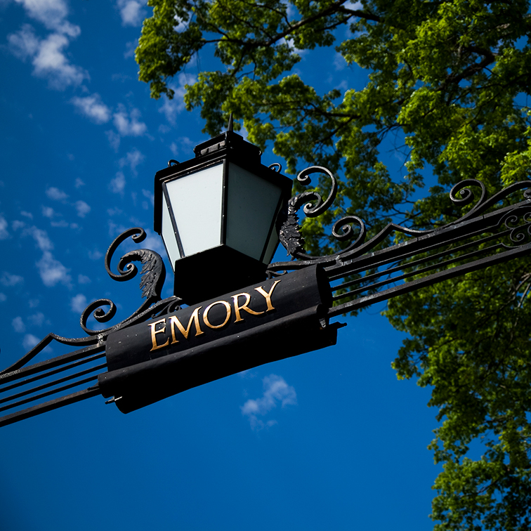the top of the main gate with the word emory and blue sky and green leaves in background