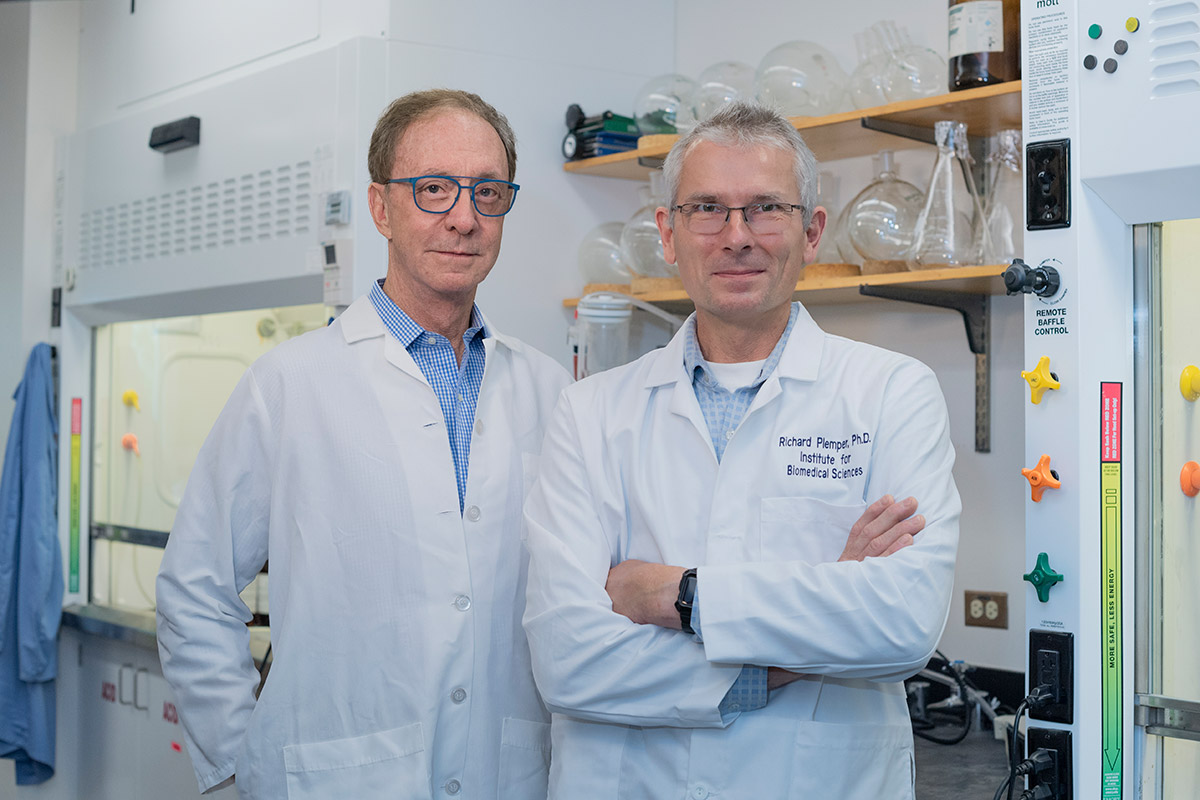 Portrait of George Painter and Richard Plemper standing together in lab coats in a research lab