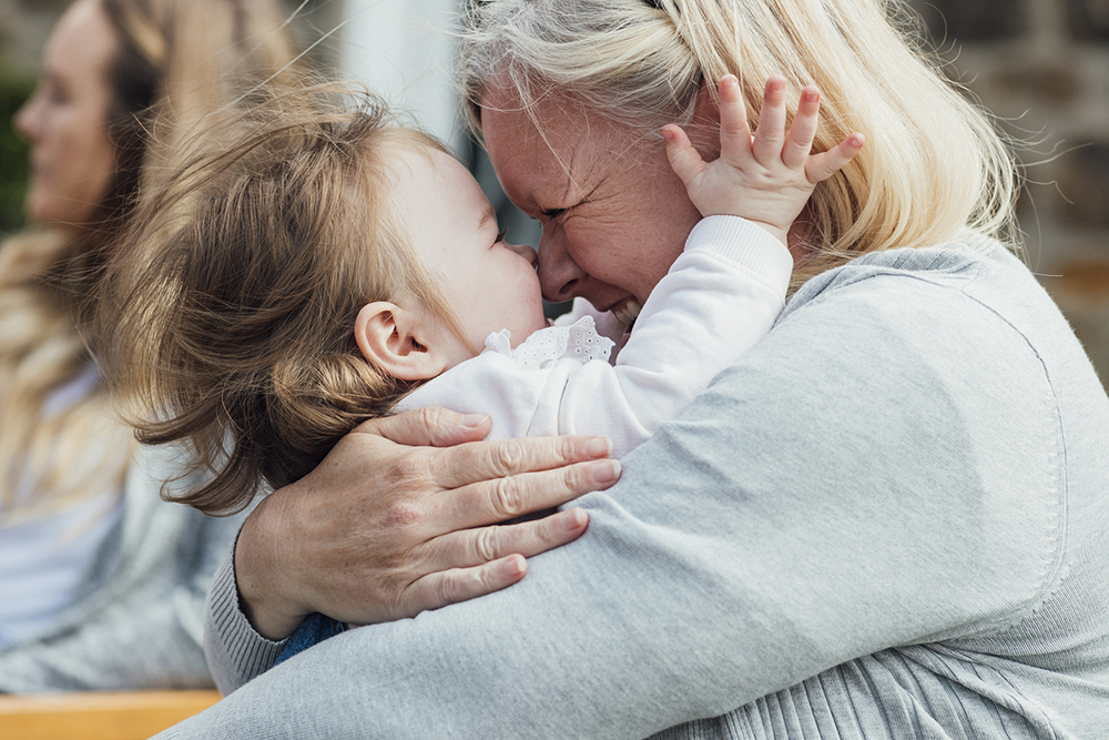 An elderly woman hugs a baby