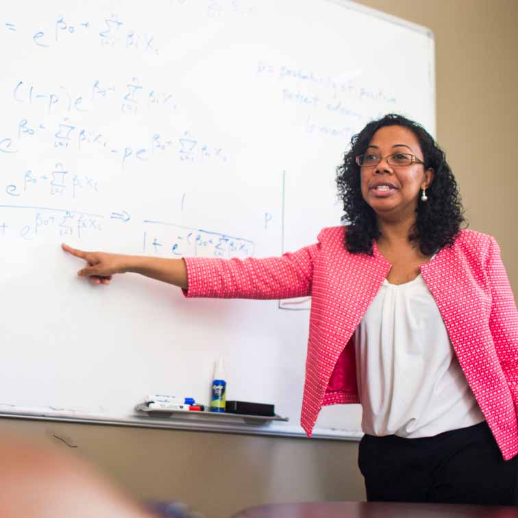 faculty member in pink jacket pointing at board