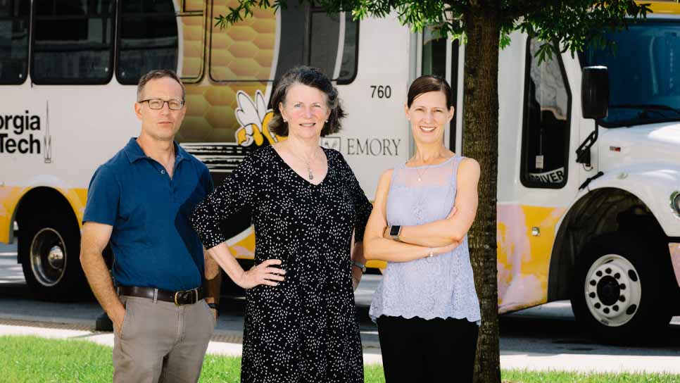three Emory faculty/staff standing in front of a Georgia Tech-Emory shuttle