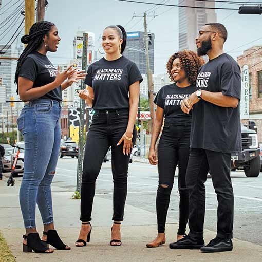 A group of people wearing Black Health Matters t-shirts standing on a sidewalk conversing